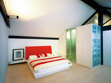 Modernes Schlafzimmer mit rot-weißer Bettwäsche Stilvolles Schlafzimmer mit schrägen Decken und bündiger Garderobe
