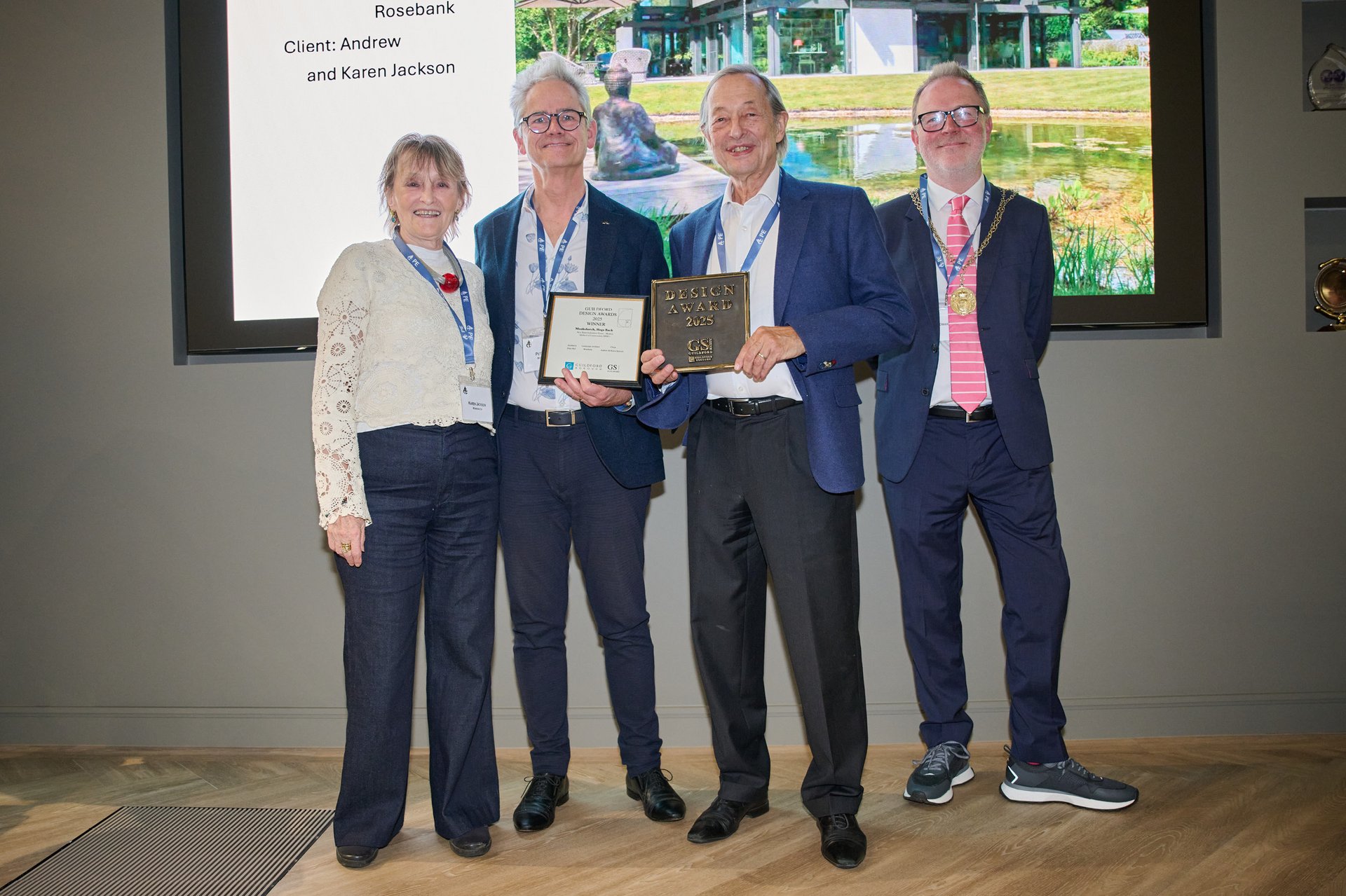 Group of four holding awards at a ceremony with a garden backdrop