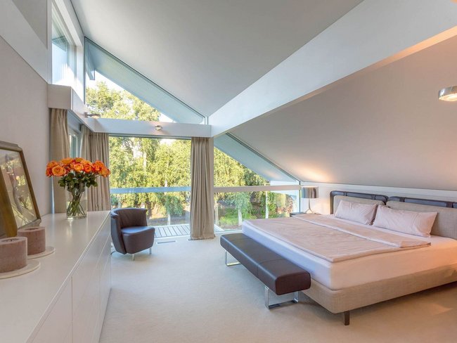 Schlafzimmer mit Doppelbett, großer Fensterfront und Blick ins Grüne