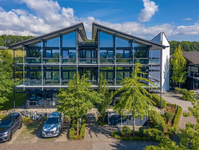Ansicht eines Bürogebäudes mit großen Fenstern und umliegendem Grün