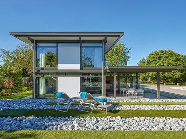 Moderne Architektur mit Glas und grünem Raum Ein stilvolles, modernes Haus umgeben von Garten und Steinen