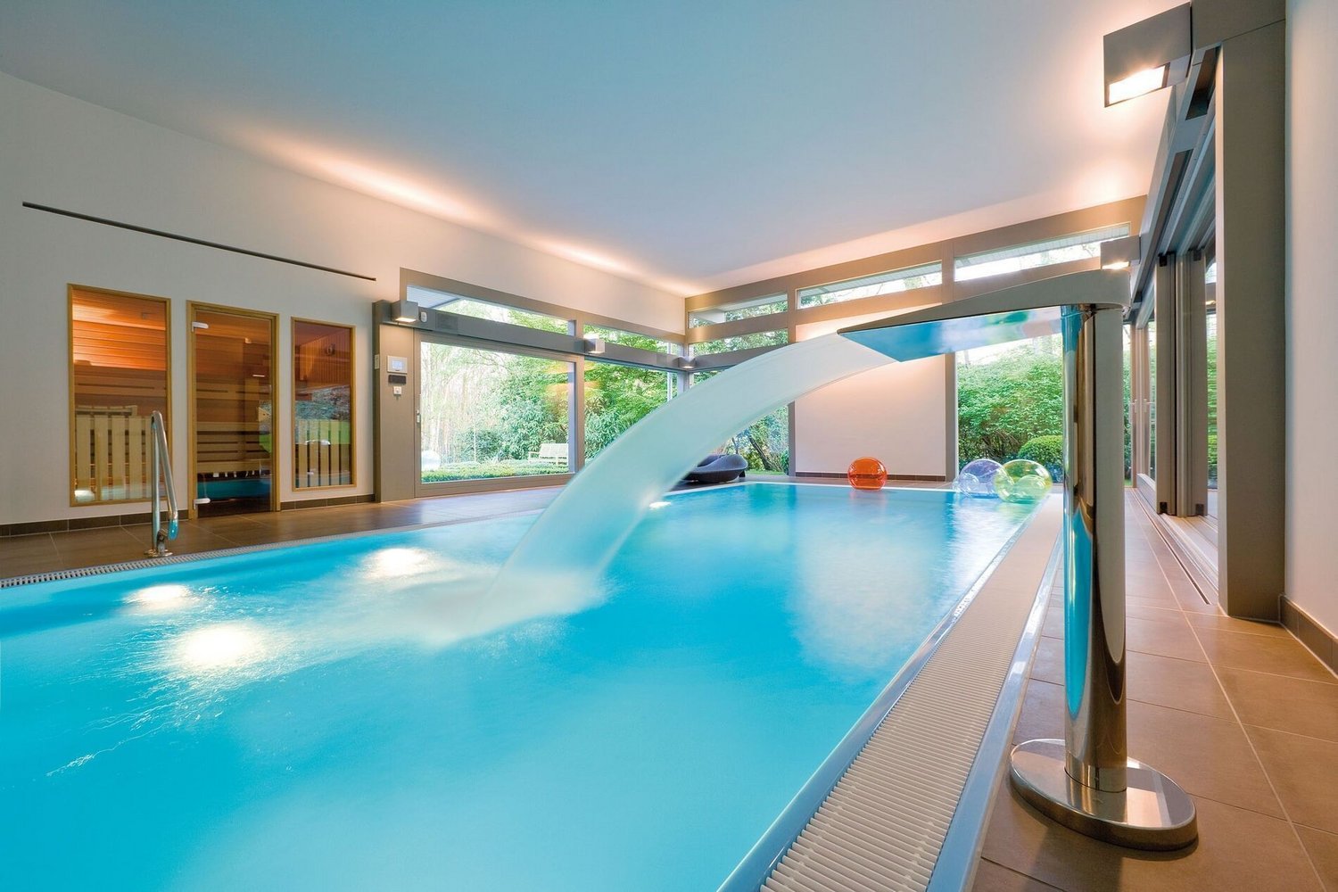 Innenansicht eines modernen Pools mit Wasserfall und Gartenblick