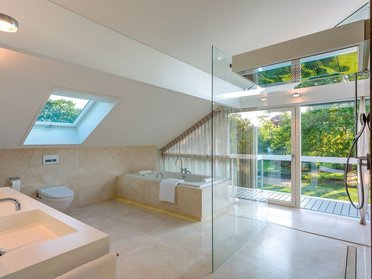 Helles Badezimmer mit Badewanne, Dusche und großen Fenstern im Grünen