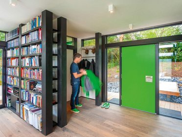 Innenraum eines modernen Fachwerkhauses mit Bücherregal und grüner Tür