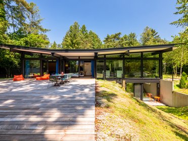Moderne Huf Bungalow mit großem Holzdeck Traumhaus umgeben von Bäumen mit modernen Glasfronten
