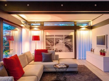 HUF Musterhaus Koblenz ebenholz 4 Gemütlicher Wohnraum mit Sofa, Tisch, Kunst und sanfter Beleuchtung