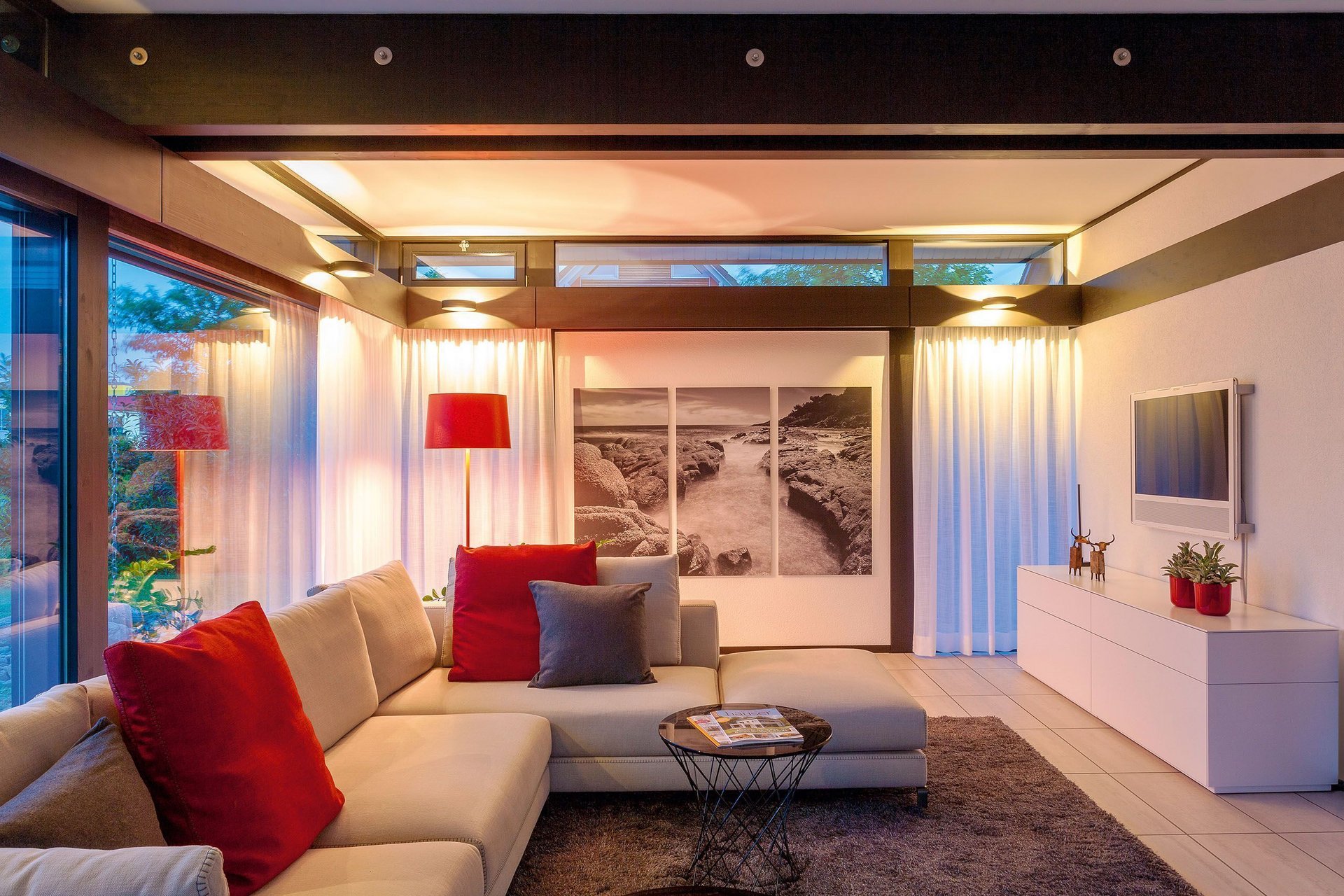 HUF Musterhaus Koblenz ebenholz 4 Gemütlicher Wohnraum mit Sofa, Tisch, Kunst und sanfter Beleuchtung