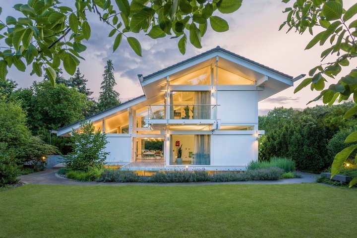 Ein helles, modernes Haus mit Garten und Bäumen im Hintergrund
