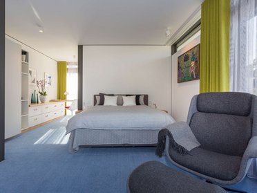 Moderner Raum mit Bett, Sessel und minimalistischer Einrichtung