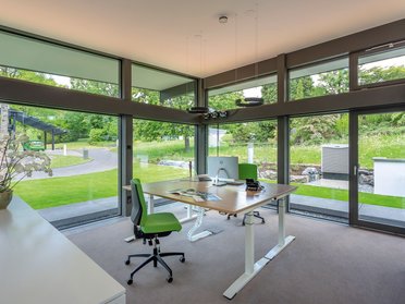 Modernes Büro mit großflächigen Fenstern und Gartenaussicht Helles Büro mit grüner Einrichtung und Blick auf die Natur