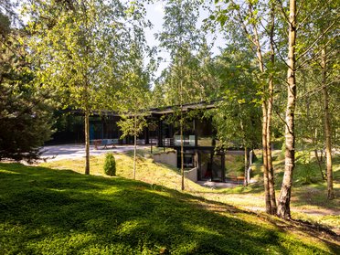 Moderne HUF-Bungalows in ländlicher Umgebung Darstellung eines modernen Bungalows umgeben von Bäumen und Grünflächen.