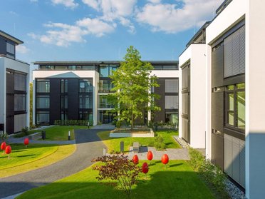 Moderne Architektur mit Pflanzen und roten Skulpturen in der Landschaft.