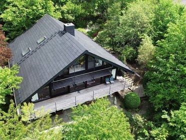 Moderne Holzarchitektur umgeben von Bäumen Ein Haus mit schwarzem Dach inmitten von grünem Laub