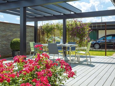 Schöner Garten mit Blütenpflanzen, Tisch und Stühlen unter Pergola