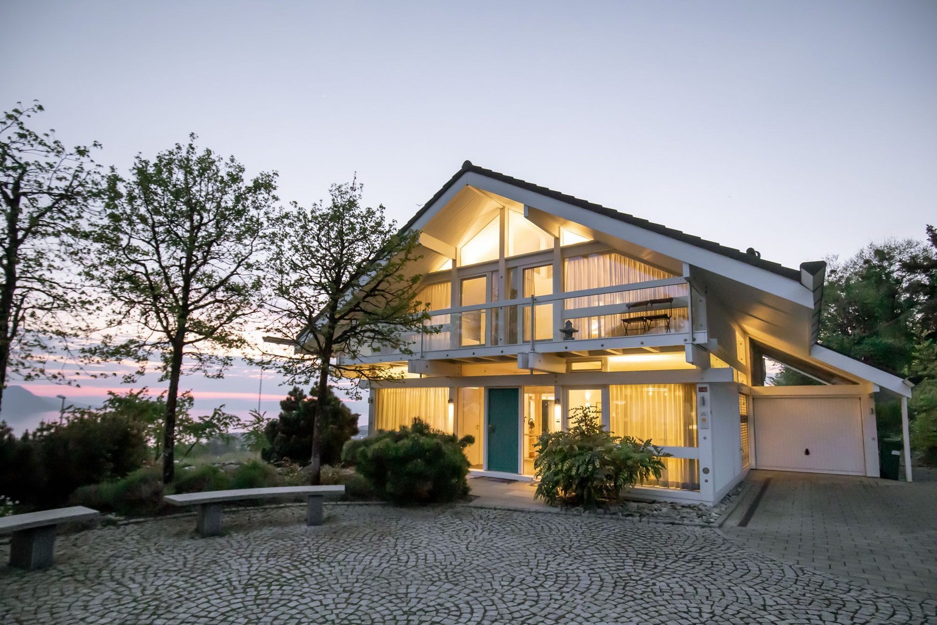 Helles modernes Haus umgeben von Bäumen und Steinweg.