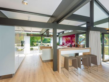 Heller Raum mit Holz- und Metallelementen, offenen Fenstern und einer Bar