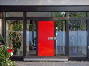 Eingangsbereich eines modernen Hauses mit Glasfront und roter Tür