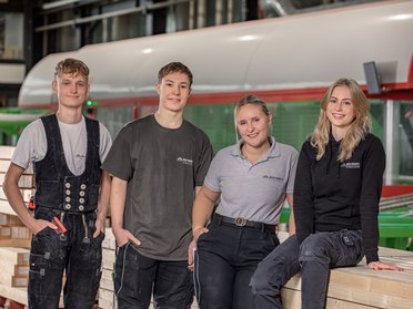 Junge Handwerker in einer Holzverarbeitungsfabrik Vier junge Personen posieren zwischen Holzstapeln in einer Fabrik