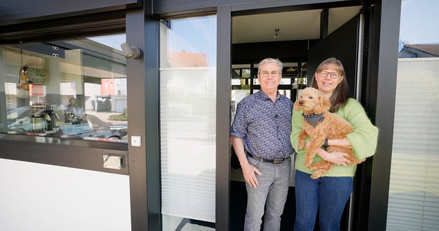 Ein Mann und eine Frau stehen mit einem Hund vor der Tür eines modernen Hauses.