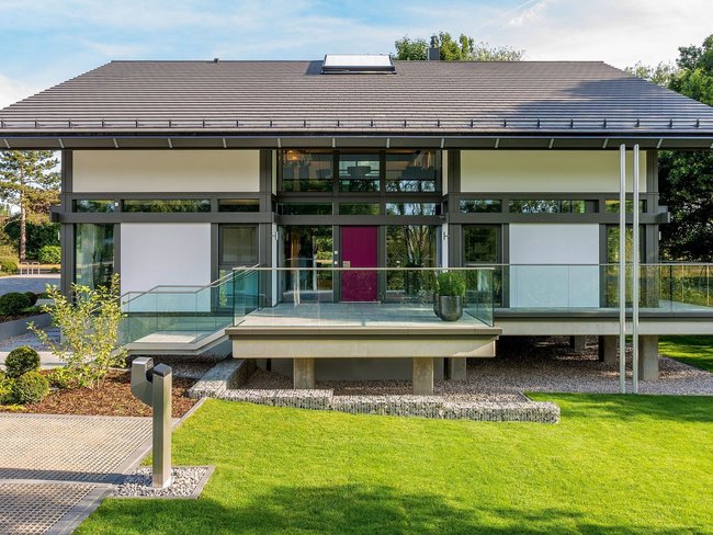 Vorderansicht eines modernen Hauses mit grüner Rasenfläche und Terrasse