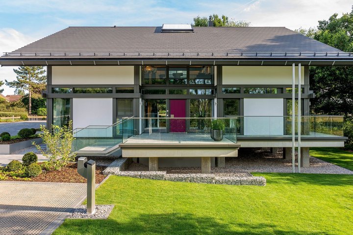 Vorderansicht eines modernen Hauses mit grüner Rasenfläche und Terrasse