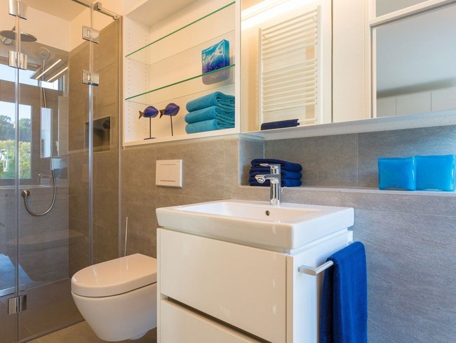 Helles Badezimmer mit Dusche, Waschbecken und blauen Handtüchern
