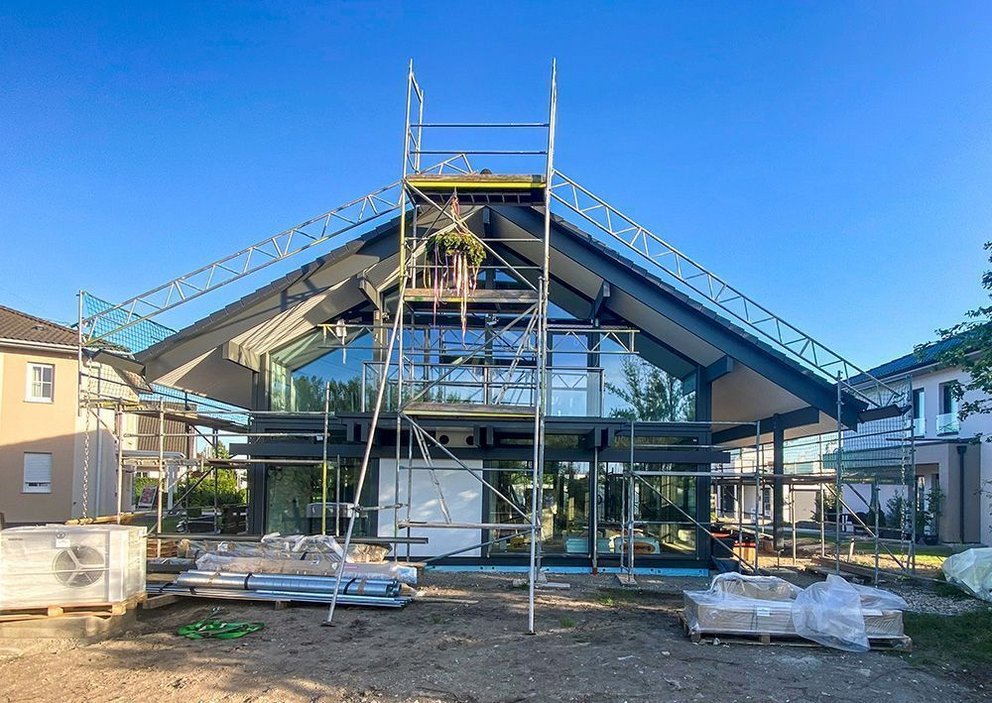 Das Bild zeigt ein im Bau befindliches Haus mit Gerüst und Baumaterialien.